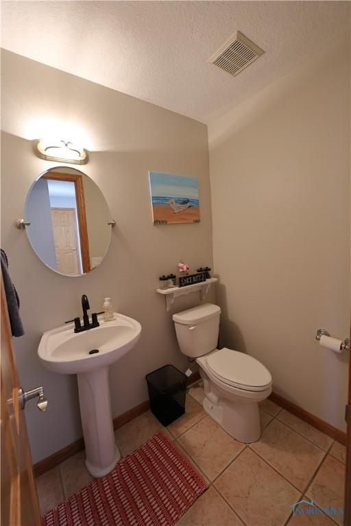 half bathroom with tile patterned floors, visible vents, baseboards, and toilet