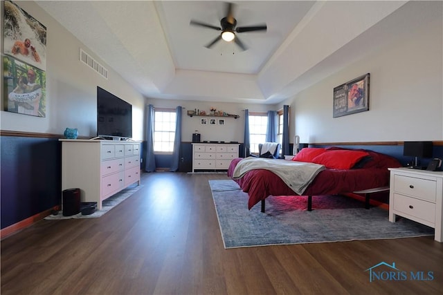 bedroom featuring wood finished floors, visible vents, baseboards, ceiling fan, and a raised ceiling