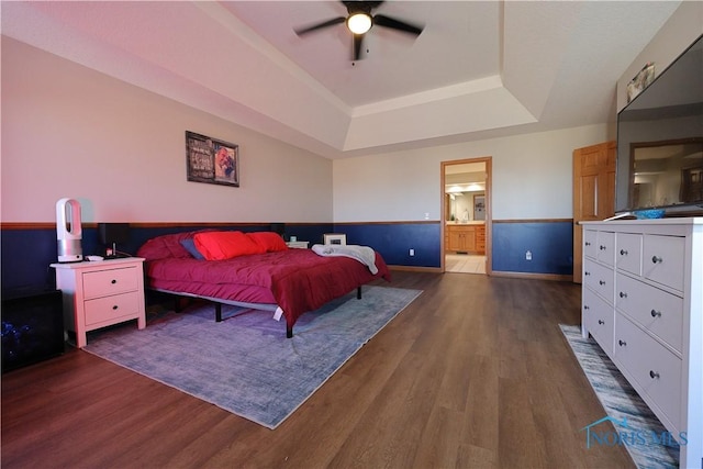 bedroom with connected bathroom, a tray ceiling, baseboards, and wood finished floors