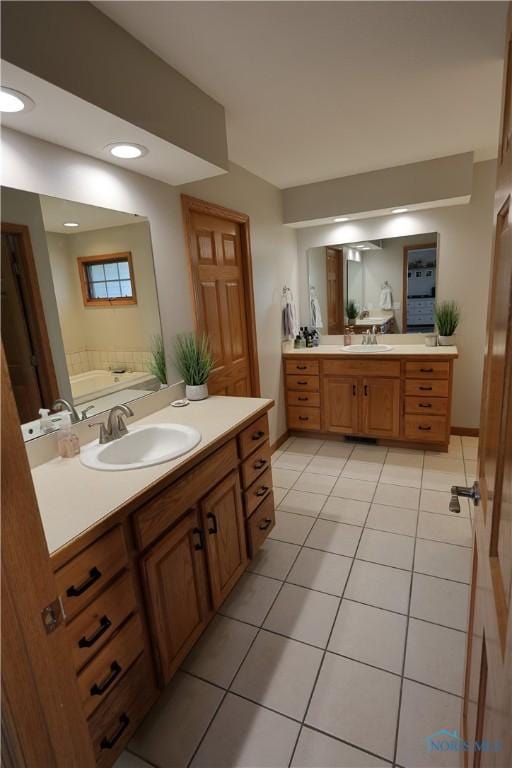 full bath with tile patterned floors, two vanities, a bath, and a sink