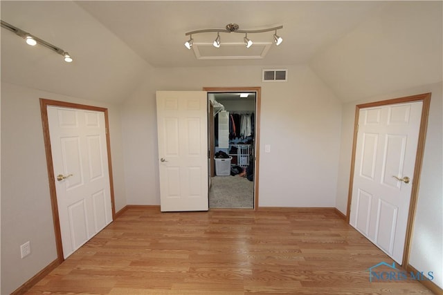 unfurnished bedroom featuring light wood finished floors, visible vents, a spacious closet, and vaulted ceiling