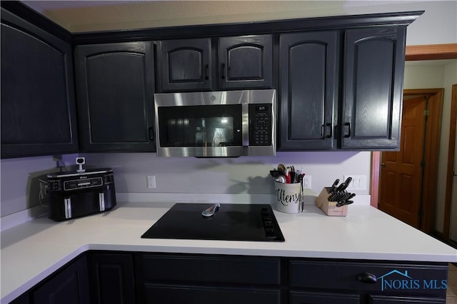 kitchen featuring stainless steel microwave, black electric stovetop, dark cabinetry, and light countertops