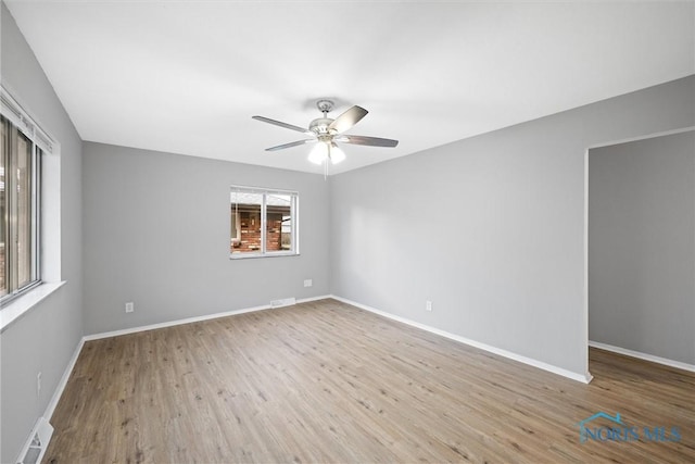 empty room featuring ceiling fan, visible vents, baseboards, and wood finished floors