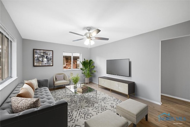 living area with a ceiling fan, baseboards, and wood finished floors