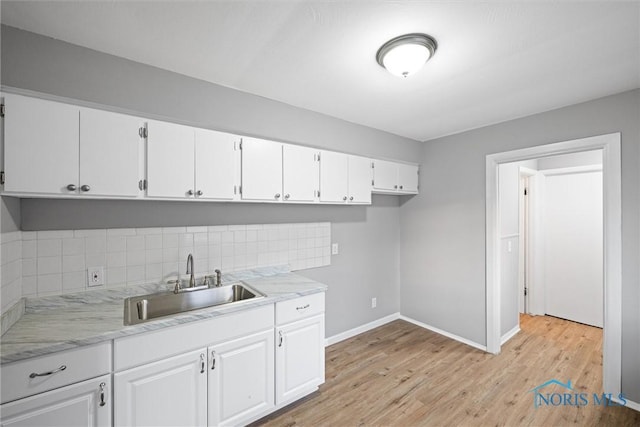 kitchen featuring tasteful backsplash, baseboards, light wood-style flooring, white cabinetry, and a sink