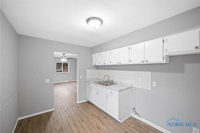 kitchen with a sink, tasteful backsplash, white cabinets, light wood finished floors, and light countertops