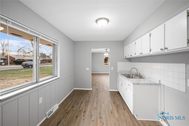 kitchen featuring visible vents, a sink, light countertops, light wood-style floors, and white cabinetry