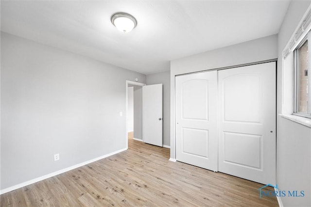 unfurnished bedroom with baseboards, light wood-type flooring, and a closet