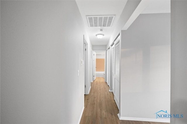 hallway with visible vents, baseboards, and wood finished floors