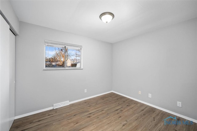 unfurnished bedroom featuring visible vents, baseboards, a closet, and wood finished floors