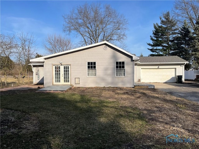 rear view of property featuring french doors, a lawn, a garage, and driveway