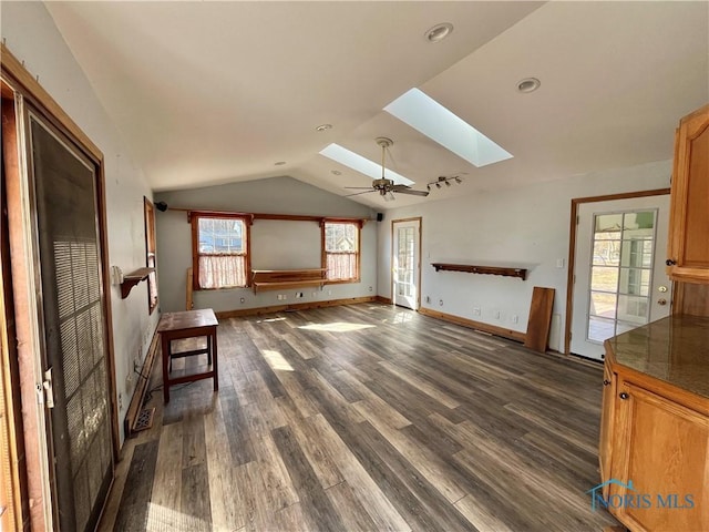 unfurnished living room featuring baseboards, vaulted ceiling with skylight, dark wood-type flooring, and ceiling fan