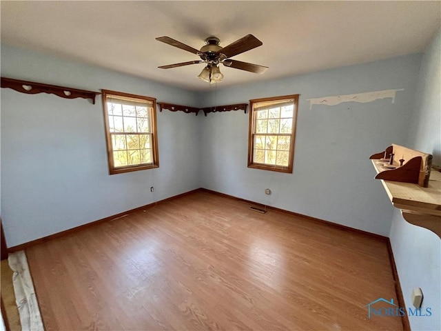 empty room with plenty of natural light, a ceiling fan, baseboards, and wood finished floors