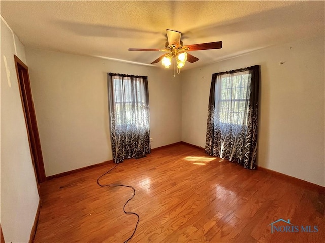 spare room featuring ceiling fan, a textured ceiling, baseboards, and wood finished floors