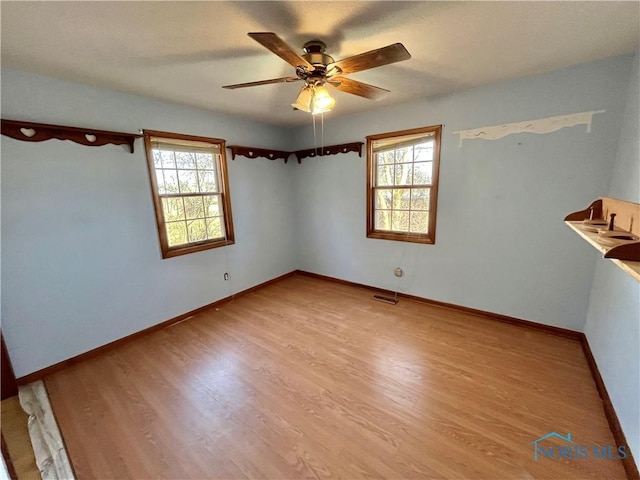 spare room featuring visible vents, baseboards, wood finished floors, and a ceiling fan