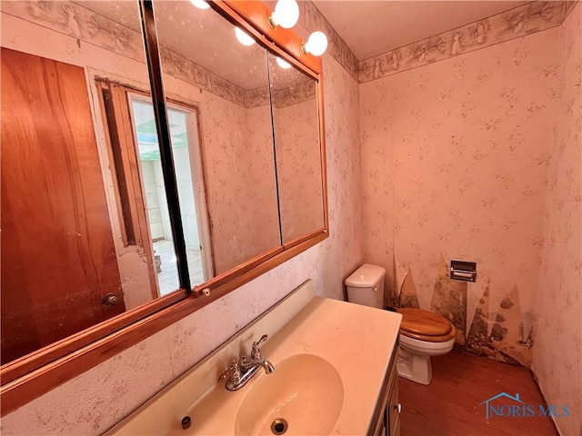 bathroom featuring toilet, wood finished floors, vanity, and wallpapered walls