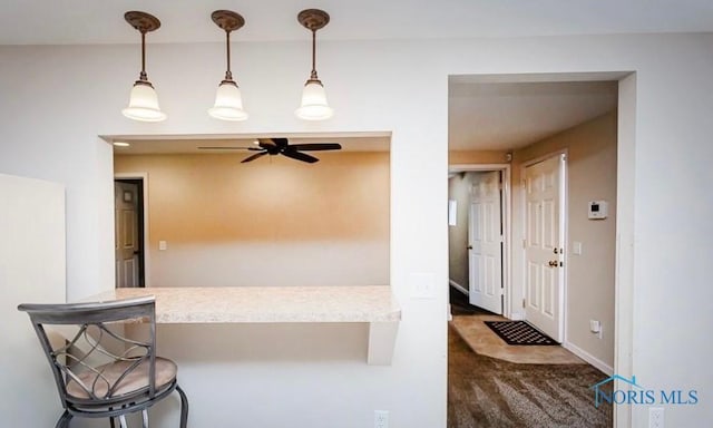 kitchen with a breakfast bar area, baseboards, a peninsula, ceiling fan, and decorative light fixtures