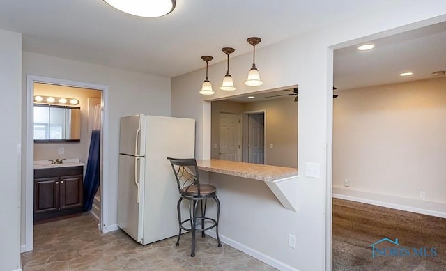 kitchen with baseboards, freestanding refrigerator, light countertops, pendant lighting, and a kitchen bar