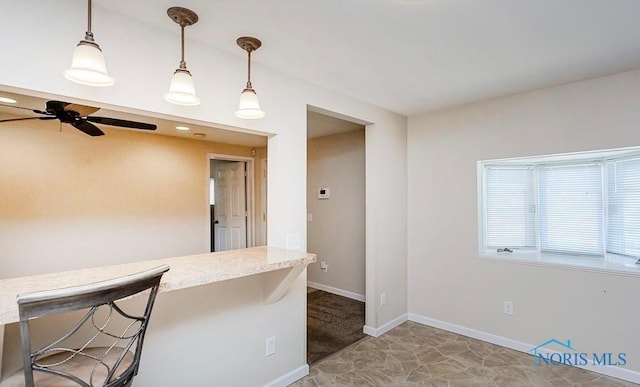 kitchen with ceiling fan, baseboards, a kitchen bar, light countertops, and hanging light fixtures