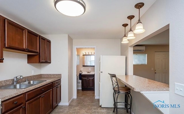 kitchen with a wall mounted air conditioner, a sink, decorative light fixtures, freestanding refrigerator, and baseboards