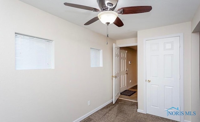 unfurnished bedroom featuring baseboards, a ceiling fan, and dark carpet