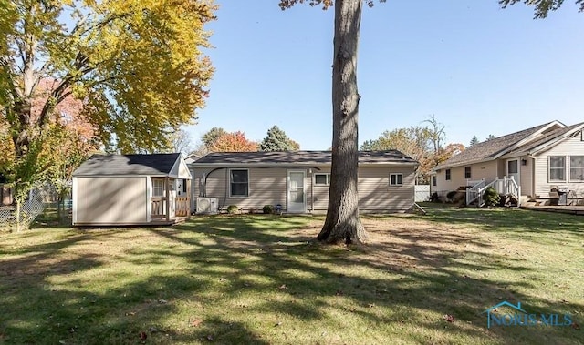 rear view of property featuring a storage shed, an outdoor structure, a yard, and fence