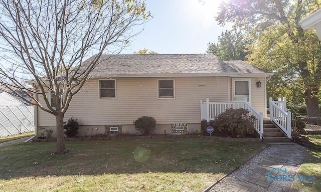 rear view of house featuring a lawn and a shingled roof