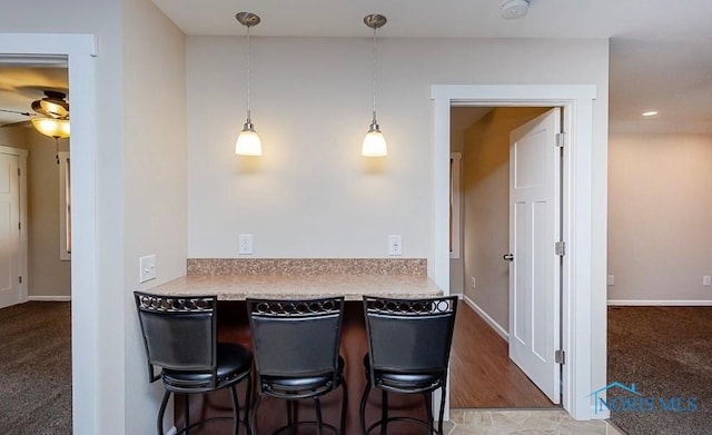 kitchen with a breakfast bar, a ceiling fan, decorative light fixtures, baseboards, and light colored carpet