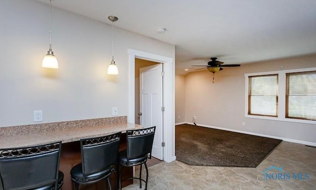 kitchen featuring baseboards, light carpet, pendant lighting, and a ceiling fan