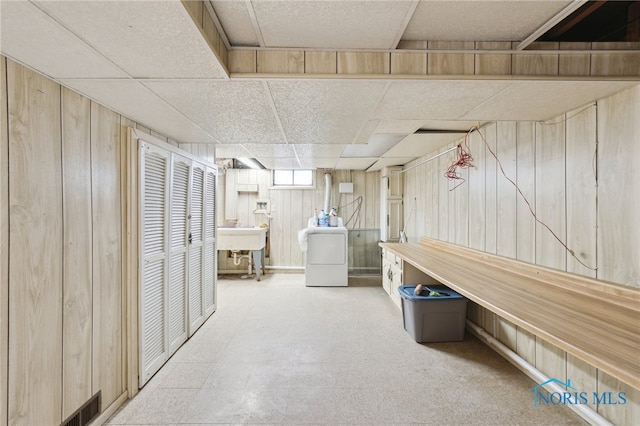 below grade area with wooden walls, visible vents, washer / clothes dryer, a paneled ceiling, and a sink