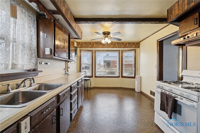 kitchen with beam ceiling, white range with gas stovetop, baseboards, and a sink