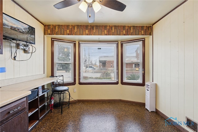 office area featuring baseboards, dark speckled floor, visible vents, ceiling fan, and wood walls