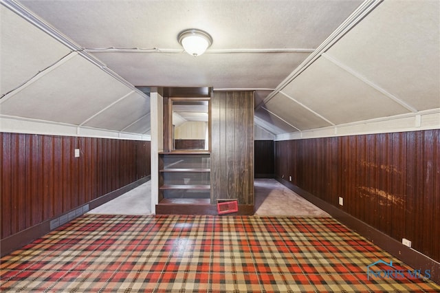 additional living space with vaulted ceiling, wooden walls, and carpet flooring