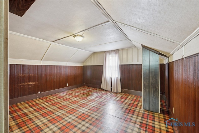 additional living space with lofted ceiling, wood walls, and a textured ceiling