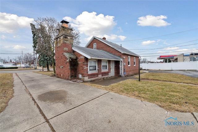 view of property exterior featuring brick siding, a chimney, a lawn, and fence