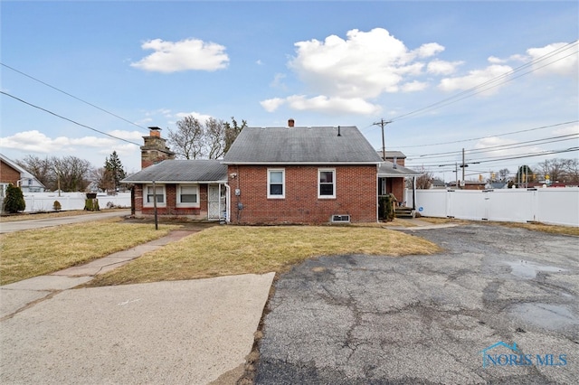 exterior space featuring a chimney, fence, brick siding, and a lawn