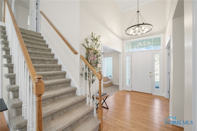 foyer featuring a notable chandelier, a high ceiling, crown molding, light wood finished floors, and baseboards