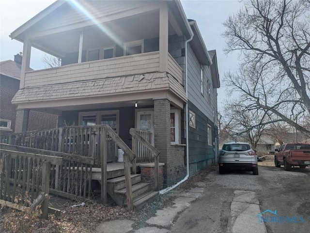 view of front of house featuring a balcony, fence, driveway, a porch, and brick siding