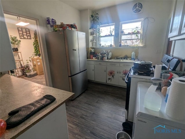 kitchen with dark wood-style floors, freestanding refrigerator, stove, white cabinets, and a sink