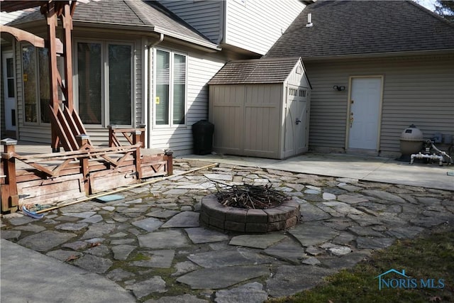 view of patio featuring an outbuilding, a storage shed, an attached garage, and an outdoor fire pit