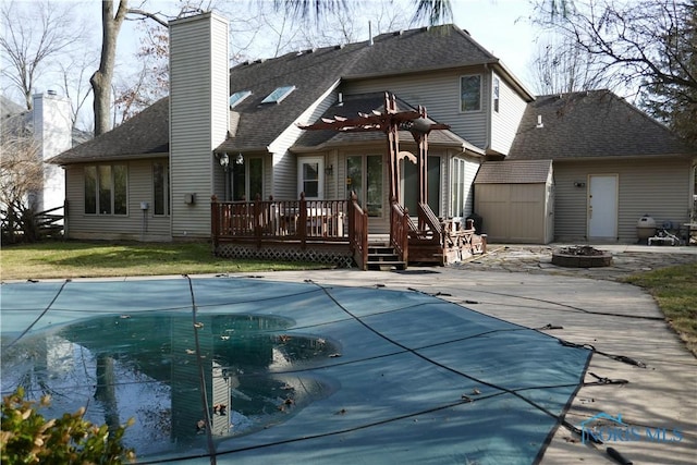 rear view of property with a covered pool, a deck, a chimney, and an outdoor fire pit