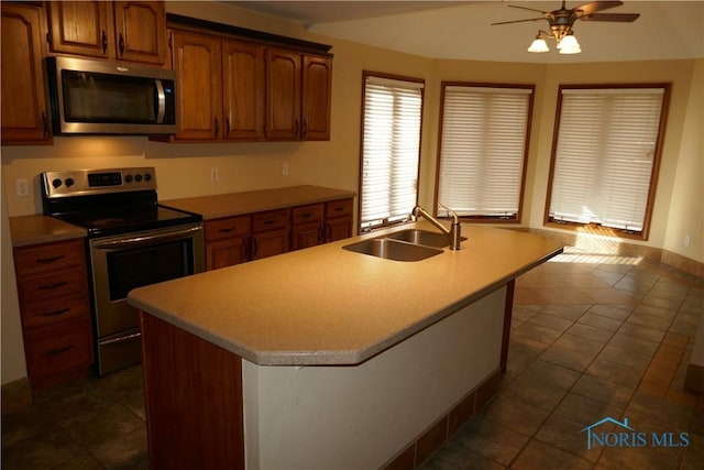 kitchen featuring dark tile patterned floors, light countertops, brown cabinets, appliances with stainless steel finishes, and a sink