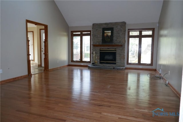 unfurnished living room featuring baseboards, a stone fireplace, wood finished floors, and vaulted ceiling