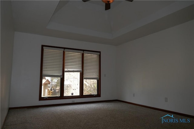 carpeted spare room featuring ceiling fan, a raised ceiling, and baseboards