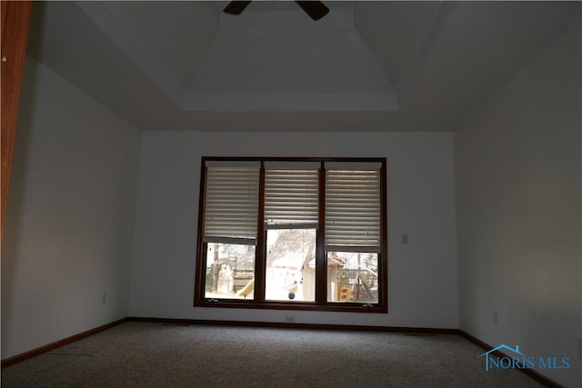 carpeted spare room with a raised ceiling, a ceiling fan, and baseboards