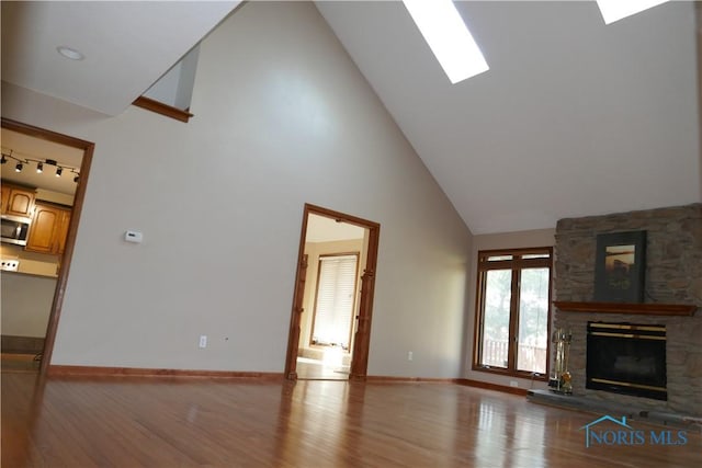 unfurnished living room with baseboards, a fireplace, a skylight, wood finished floors, and high vaulted ceiling