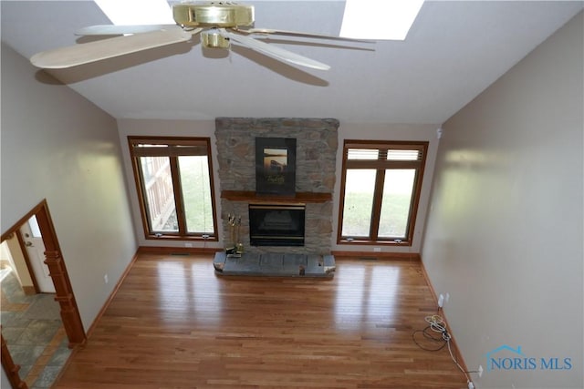 unfurnished living room with a stone fireplace, lofted ceiling, wood finished floors, and baseboards