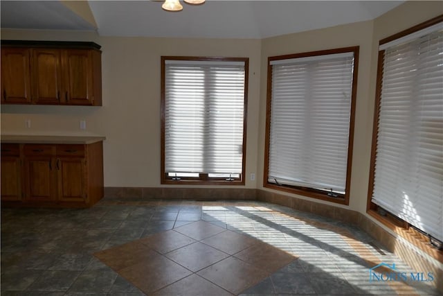 unfurnished dining area with baseboards and dark tile patterned floors