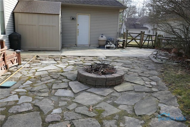 view of patio featuring a gate, a fire pit, an outbuilding, and fence