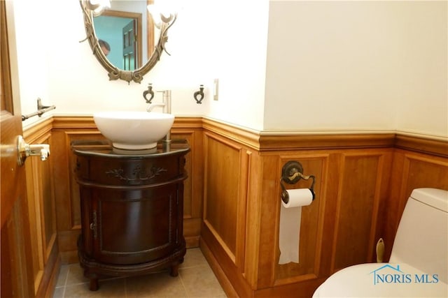 half bath featuring tile patterned flooring, wainscoting, toilet, and vanity